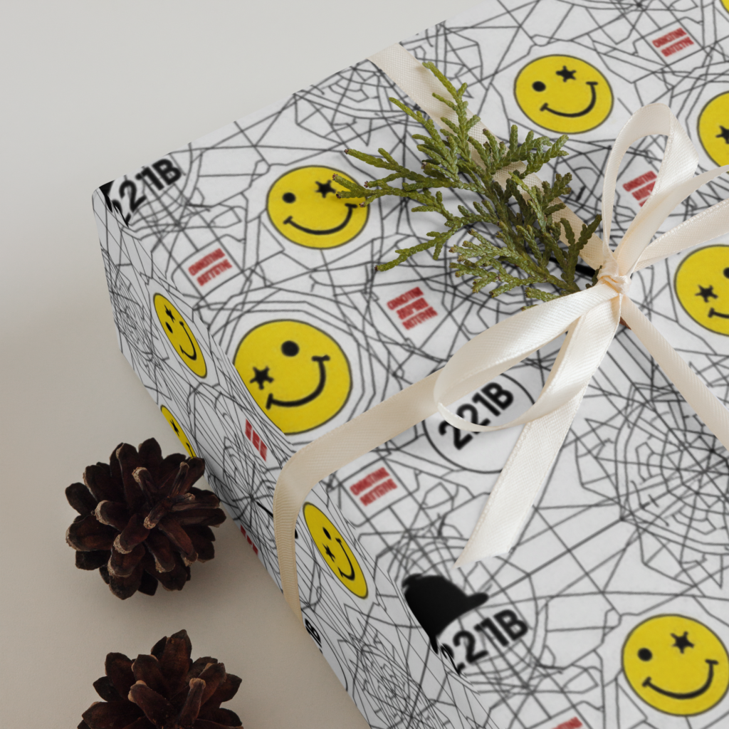 Square gift box wrapped in white paper with smiley faces, doodle-style icons, and grid patterns, tied with white ribbon.
