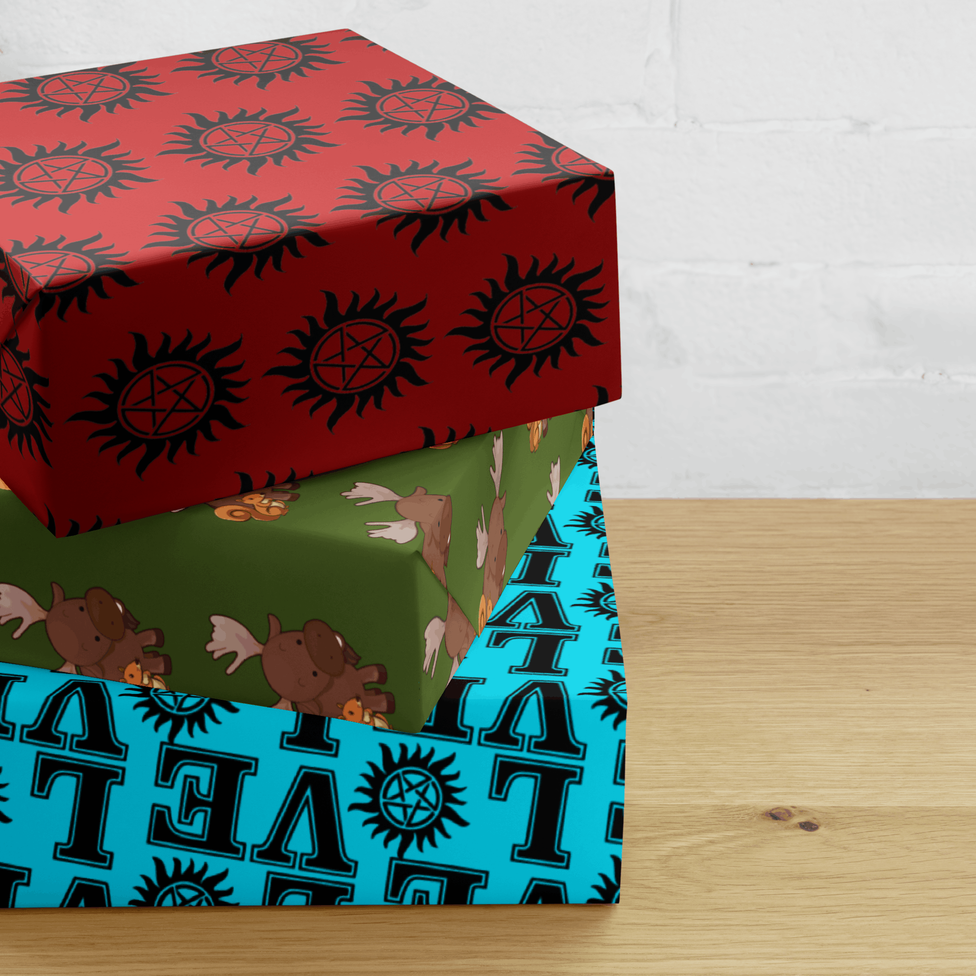 Three stacked gift boxes wrapped in patterned paper, featuring red and teal designs with repeating graphic symbols, displayed on a wooden surface.